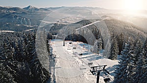 Sun ski resort at snow mountain forest aerial. Escalator chair at pine trees. Tourist active sport