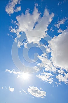 Sun sparkling in blue sky with fluffy clouds