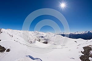 Sun star glowing over snowcapped mountain range and high mountain peaks in the italian alpine arc, in a bright sunny day of winter