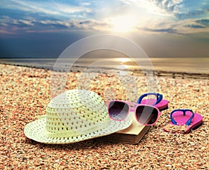 Sun straw hat, book, flip flop sandals and sunglasses lying on the beach