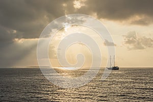 Sun at sunset shining through a picturesque clouds over the Indian ocean with Maldivian islands and ship with masts