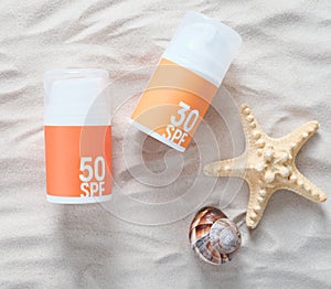 Sun tan protection creme bottles on a sand next to starfish and seashell. summer skin care concept. orange and yellow pump bottles