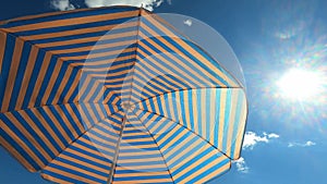 Sun umbrella in blue and yellow stripes sways in the wind against the sky