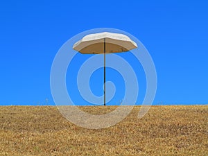 Sun umbrella on dry lawn against blue sky