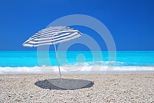 Sun umbrella on a pebble beach with turquoise sea