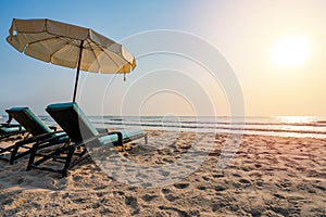 Sun umbrellas and chairs on tropical beach with sunset