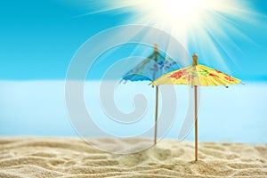 Sun umbrellas on sandy beach with blurry blue ocean,  sky and sun beams. Summer background. Soft focus