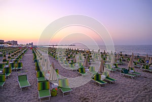 sun umbrellas and sun beds on the beach across sunset sky. Summer vacation background. Senigallia, Italy