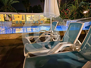 Sun umbrellas, sun loungers and a pool of warm clear water at the all-inclusive hotel at night in a warm tropical oriental