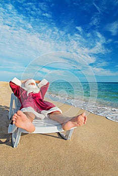 Sunbathing Santa Claus relaxing in bedstone on tropical beach