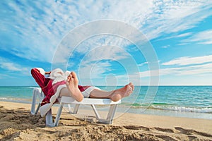 Sunbathing Santa Claus relaxing in bedstone on tropical beach