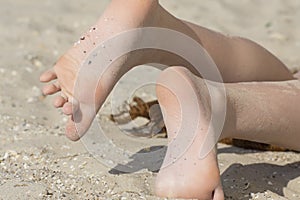 Sunbathing on a sunny beach. Girl`s heels in the sand and shells. Holidays at sea