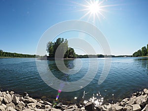 Sunbeam in blue sky and flares at lakeside