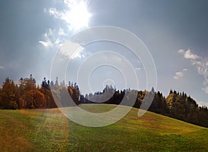 Sunbeam over a green meadow and fir trees in autumn panorama
