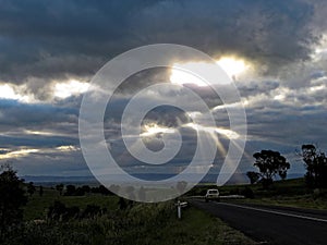 Driving in Australian countryside by sun rays through cloud gaps