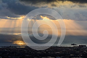 Sunbeams over the city. Sun cuts through the clouds over the sea