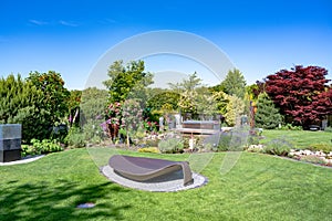 Sunbed in beautiful garden with lavender, pinks, allium, roses flowering in garden creek and pond