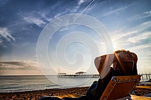 Sunbed on the sand beach, man on it and view to water of sea, pierce and blue sky with white clouds in a nice day, morning or