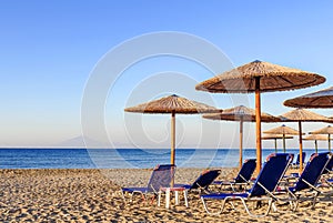 Sunbed, straw umbrella on beautiful rising sun beach background