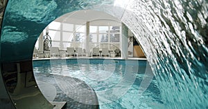 Sunbeds in the indoor swimming pool. Move camera through the waterfall