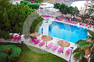 Sunbeds and parasols on wooden deck nearby swimming pool