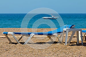 Sunbeds on rocky beach and parasailing speed boat waiting for customers