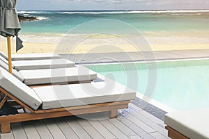 Sunbeds on Swimming Pool Wooden Deck with White Sand Beach and Blue Sea Background