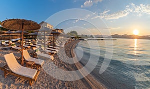 Sunbeds and umbrella on the beach at sunset time, Corfu Island, Greece