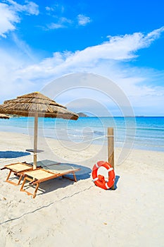 Sunbeds with umbrella and lifesaver ring on white sand beach in Porto Giunco bay, Sardinia island, Italy