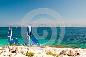 Sunbeds and umbrellas (parasols) on rocky beach in Corfu Island