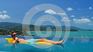 Sunburnt man on mattress in swimming pool drinking beverage from metal can