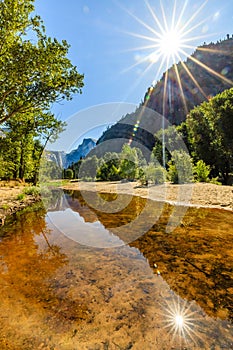 Sunburst in the sky and from the smooth Merced river looking towards half dome on the horizon in Yosemite National Park