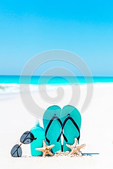 Suncream bottles, goggles, starfish and sunglasses on white sand beach background ocean