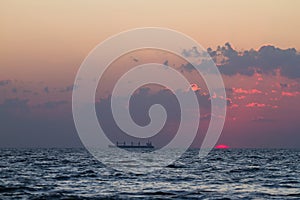 Sundawn on the Black Sea, sun disk appear on horizon with some clouds, early morning, gentle waves on water surface, cargo ship