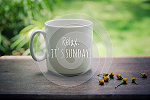 Sunday mug of coffee concept. Morning white coffee with text on it - Relax. It is Sunday, and yellow little flowers arrangement.