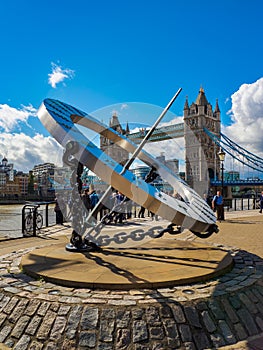 The sundial at St. Katharine docks and Tower Bridge over the River Thames in London, UK on a sunny day.