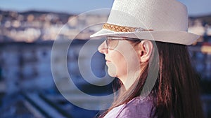 Sundown Serenity: Woman in Sun Hat and Sunglasses Watching Cityscape from Balcony