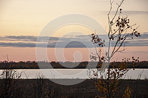 Sundown and sunrises. Blue sky with tints of purple and much clouds. Silhouettes of trees and grass are reflectioning in the river