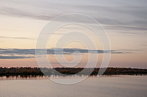 Sundown and sunrises. Blue sky with tints of purple and much clouds. Silhouettes of trees and grass are reflectioning in the river