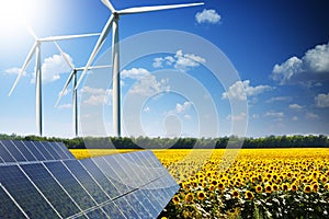 Sunflower field reflected on photovoltaic panels against wind turbines, concept of renewable energy from the nature