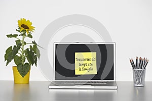 Sunflower plant on desk and sticky notepaper with Italian text on laptop screen saying Trascorrere del tempo con la famiglia photo