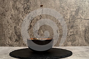 Sunflower seeds falling into a ceramic bowl with more salted sunflower seeds on a gray background