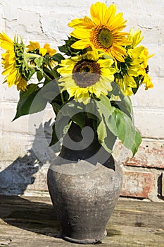 Sunflowers in vintage clay jug on wooden table