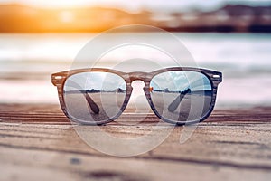 A sunglass on wooden board on blur beach with bokeh background