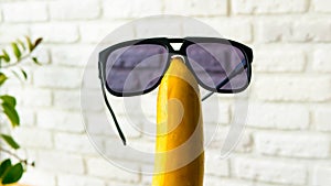 Sunglasses on a banana on a brick wall background,close-up.Cheerful fruit with glasses.