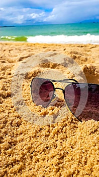 sunglasses on the beach sand with the sea and sky in the background.