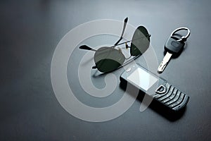 Sunglasses, car key and cellphone on a wooden table