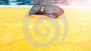 Sunglasses closeup summer background. Beach pool equipment with travel sunglasses on yellow holiday towel. Outdoor relax