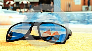 Sunglasses closeup summer background. Beach pool equipment with travel sunglasses on yellow holiday towel. Outdoor relax