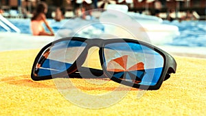 Sunglasses closeup summer background. Beach pool equipment with travel sunglasses on yellow holiday towel. Outdoor relax